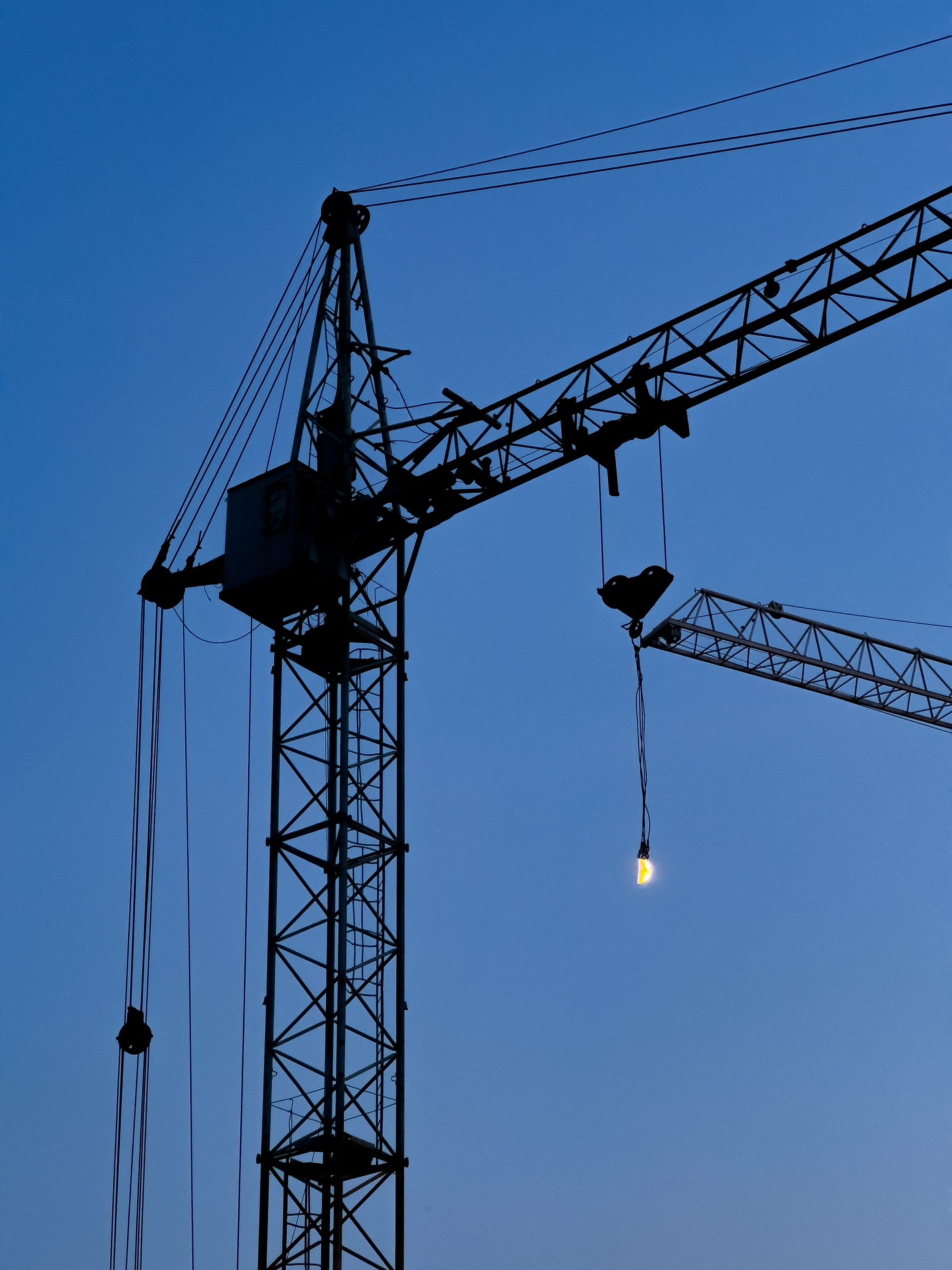 A tower crane in silhouette against a deep blue twilight sky